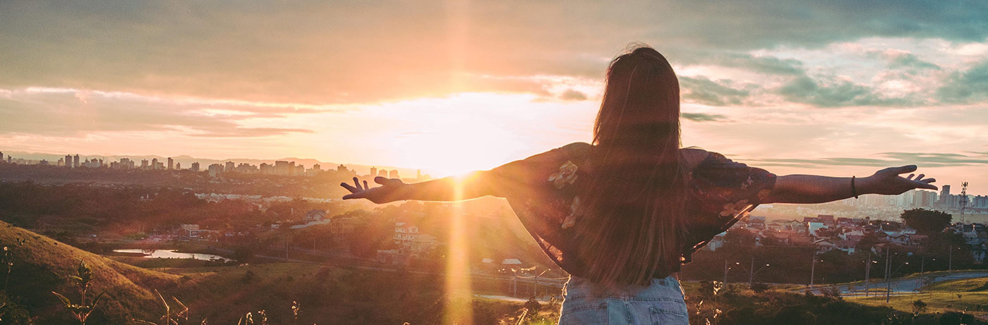 femme levant les bras au ciel devant un couche de soleil