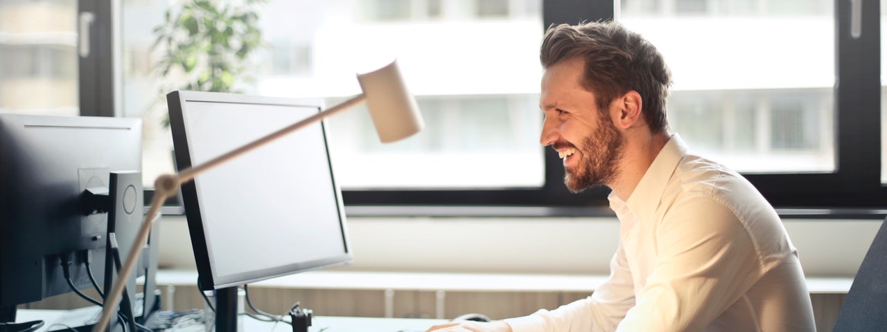 Homme souriant devant son écran d'ordinateur